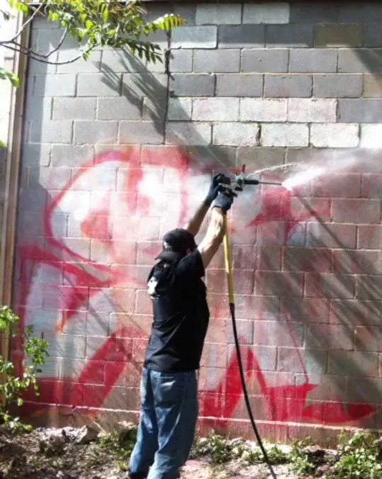 man removing graffiti with a power washer